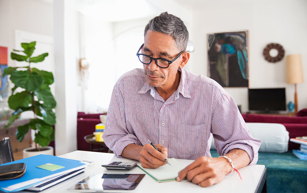 A senior man is sitting at his dining room table, working on finances.