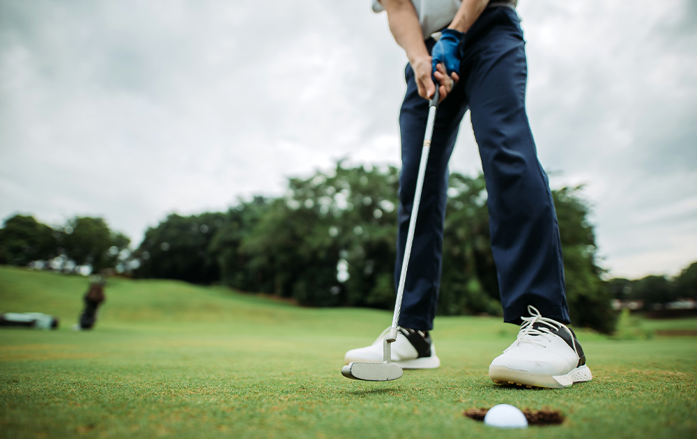 A golfer prepares to putt on a green, low-angle view highlighting the putter and ball.