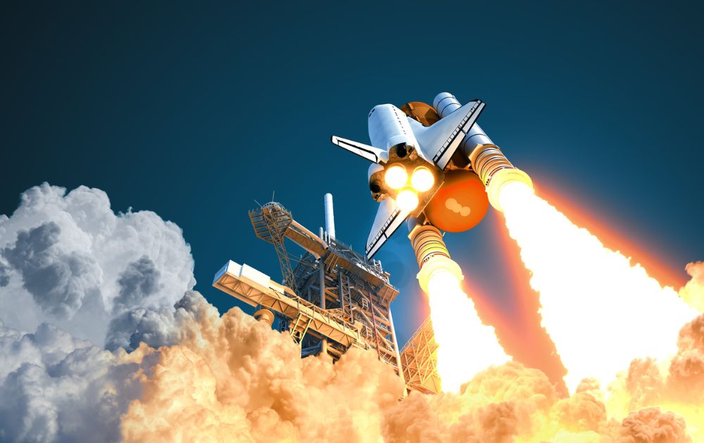 A space shuttle lifts off from a launchpad, propelled by massive plumes of fire and smoke against a deep blue sky.